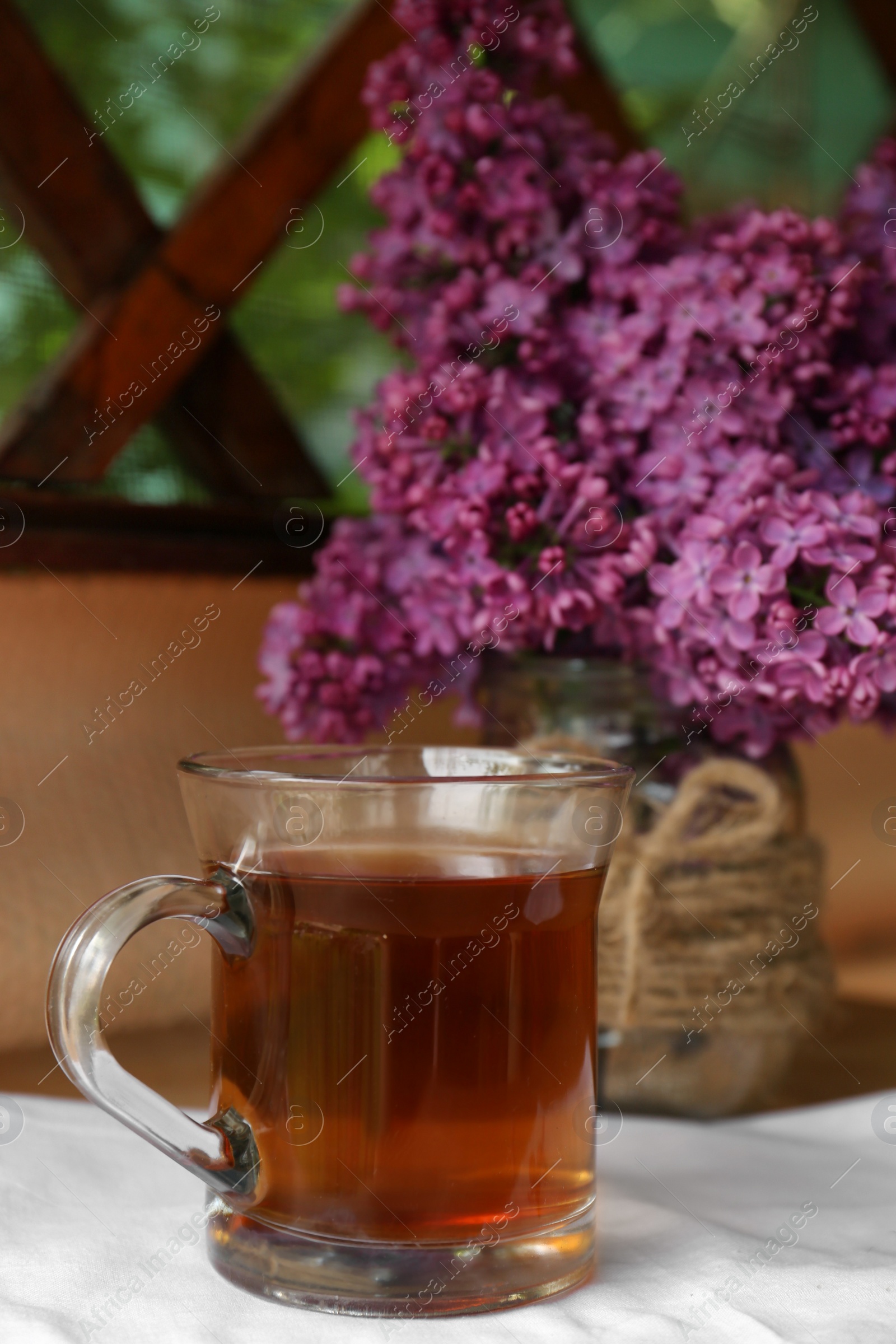 Photo of Bouquet with beautiful lilac flowers and glass cup of tea on wooden table indoors