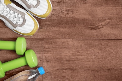 Vinyl dumbbells, sneakers and bottle of water on wooden background, flat lay. Space for text