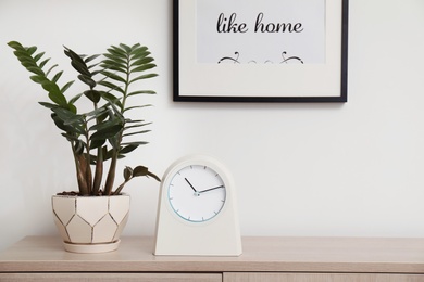 Modern clock on chest of drawers against light background