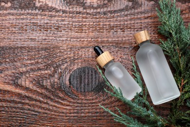 Bottles of juniper essential oil and fresh twigs on wooden table, flat lay. Space for text