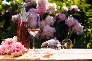 Photo of Bottle and glass of rose wine near beautiful peonies on wooden table in garden. Space for text
