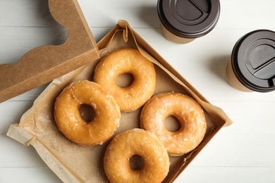 Photo of Delicious donuts in box and coffee on white table, flat lay