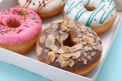 Photo of Box with different tasty glazed donuts on light blue background, closeup