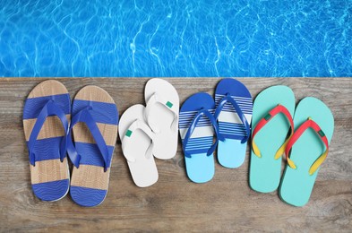 Image of Pairs of flip flops on wooden deck near swimming pool, flat lay 