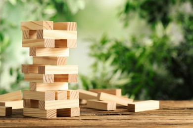 Photo of Jenga tower made of wooden blocks on table outdoors, space for text