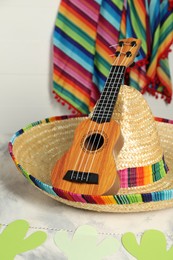 Photo of Mexican sombrero hat and ukulele on grey textured table, closeup