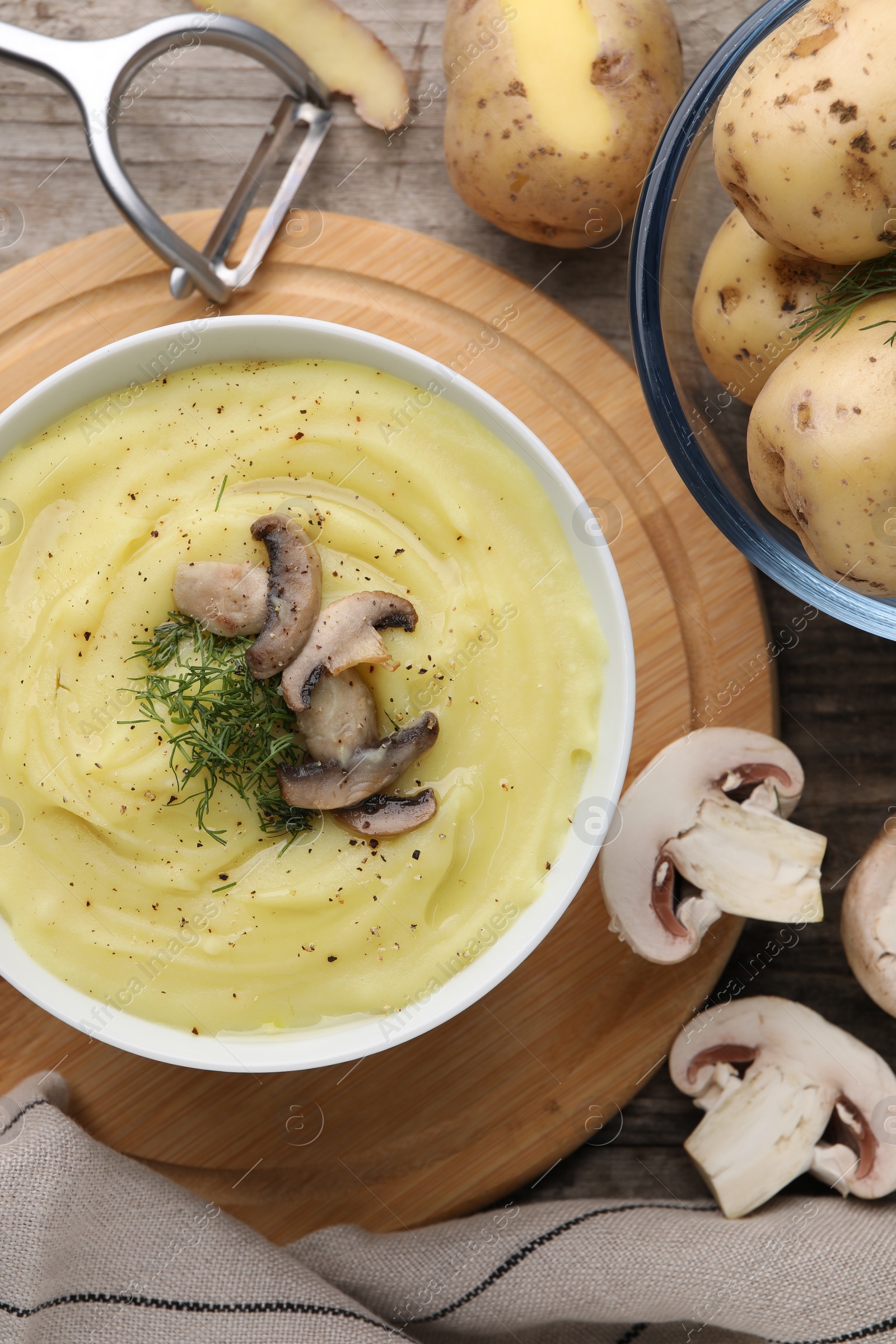 Photo of Bowl of tasty cream soup with mushrooms, dill and raw potatoes on wooden table, flat lay