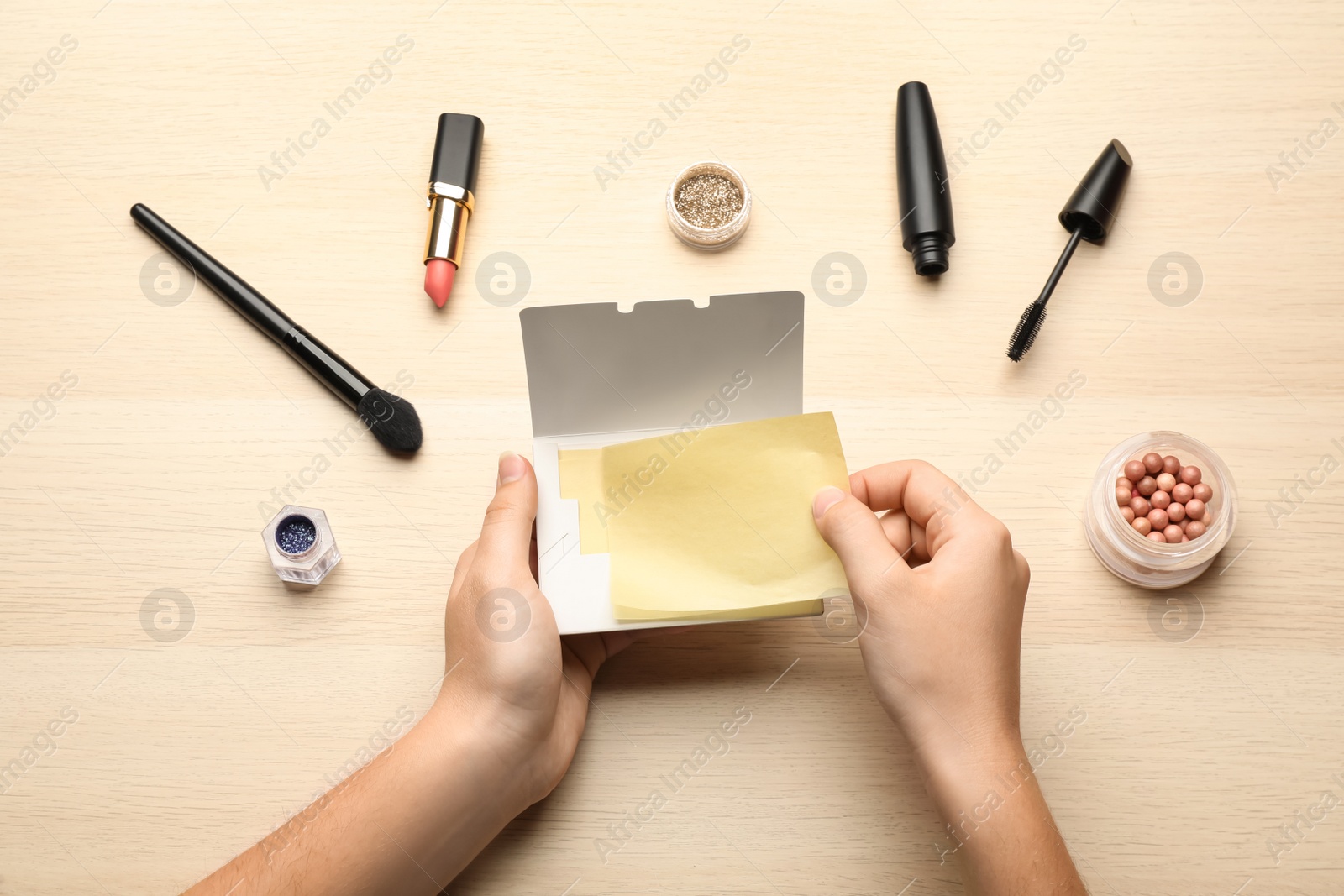 Photo of Woman with package of oil blotting tissues and decorative cosmetics at wooden table, top view. Mattifying wipes