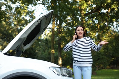Stressed young woman talking on phone near broken car outdoors