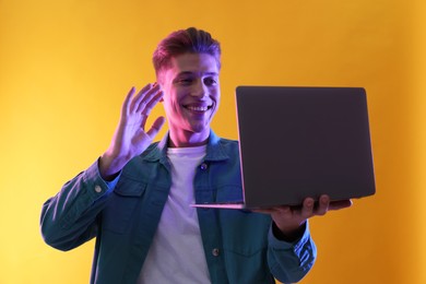 Photo of Young man with laptop talking via video chat on yellow background