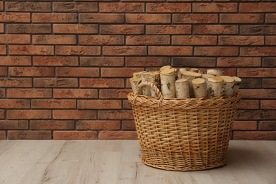 Wicker basket with firewood near brick wall indoors, space for text