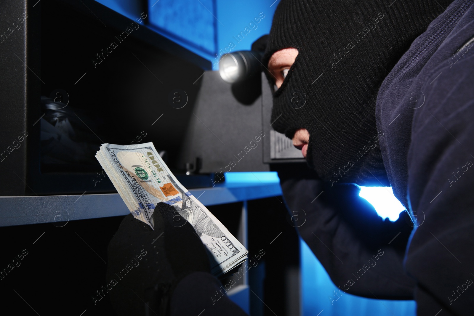 Photo of Thief taking money out of steel safe indoors at night, closeup