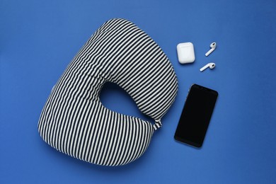 Photo of Striped travel pillow, smartphone and earphones on blue background, flat lay