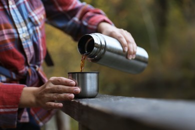 Photo of Woman pouring hot drink from metallic thermos into cup lid outdoors, closeup