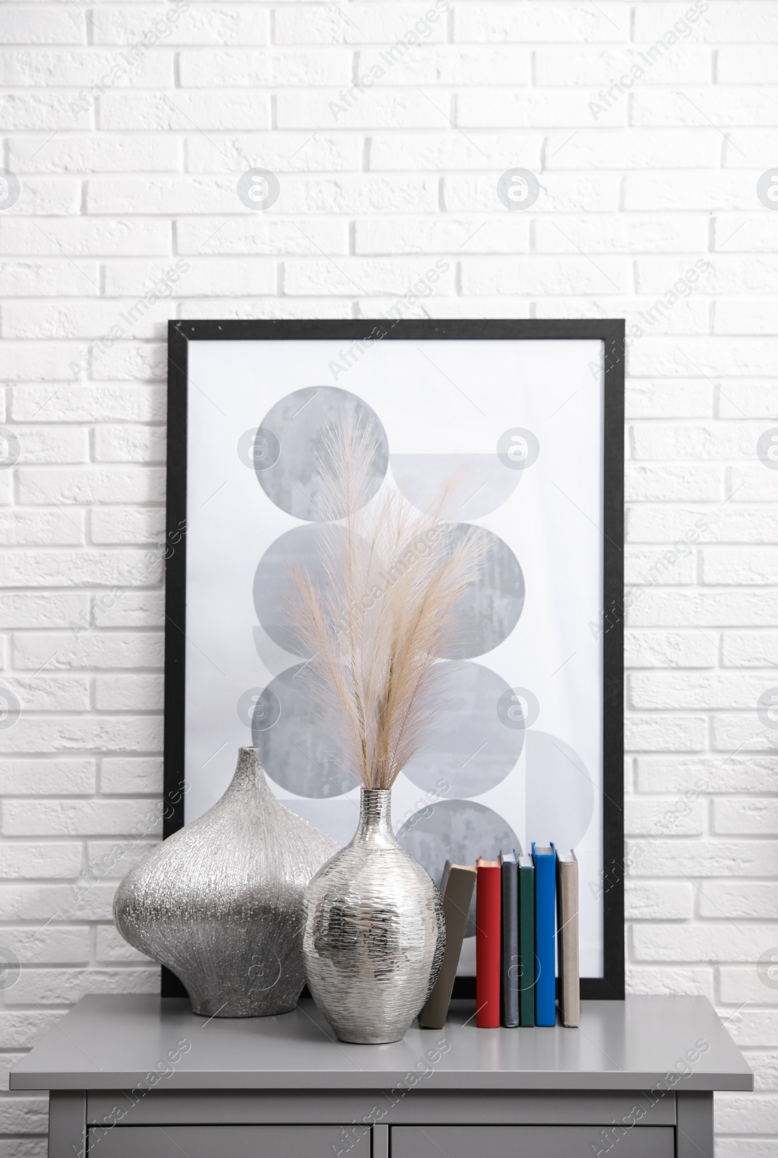 Photo of Grey chest of drawers with decor and books near white brick wall. Interior design