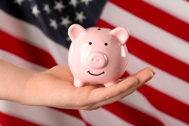 Woman holding piggy bank against American flag, closeup