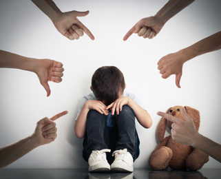 Image of People bullying sad little boy near white wall
