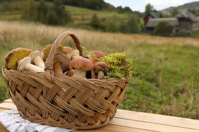 Photo of Wicker basket with fresh wild mushrooms on wooden table outdoors, space for text