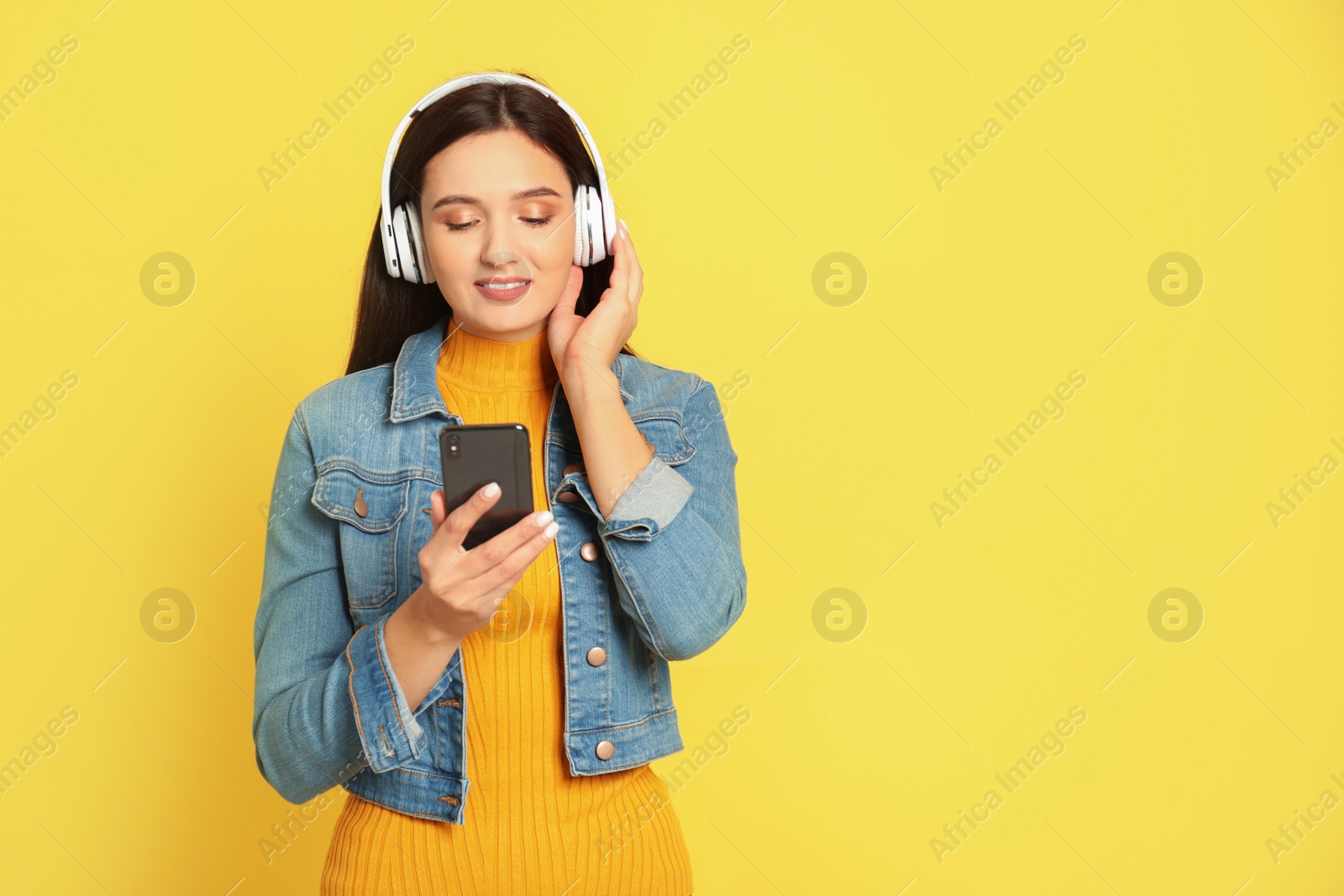 Photo of Young woman listening to audiobook on yellow background. Space for text