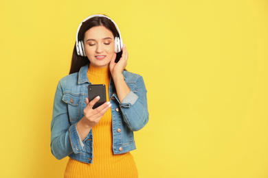 Young woman listening to audiobook on yellow background. Space for text