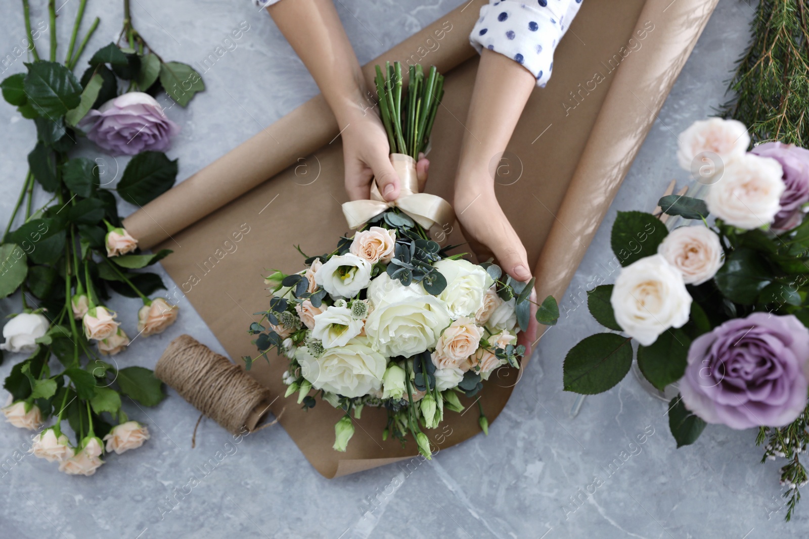 Photo of Florist making beautiful wedding bouquet at light grey marble table, top view