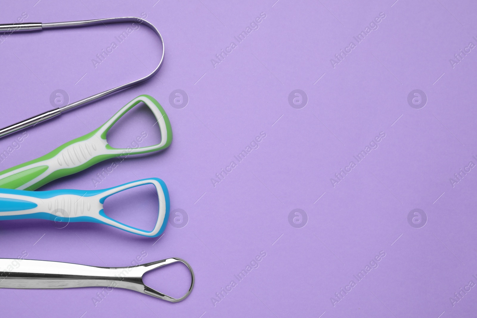 Photo of Different tongue cleaners on violet background,flat lay. Space for text