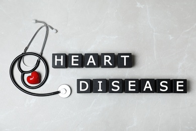 Wooden cubes with text Heart Disease and stethoscope on grey background, flat lay