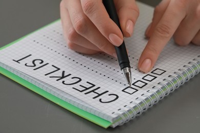 Woman filling Checklist with pen at grey table, closeup