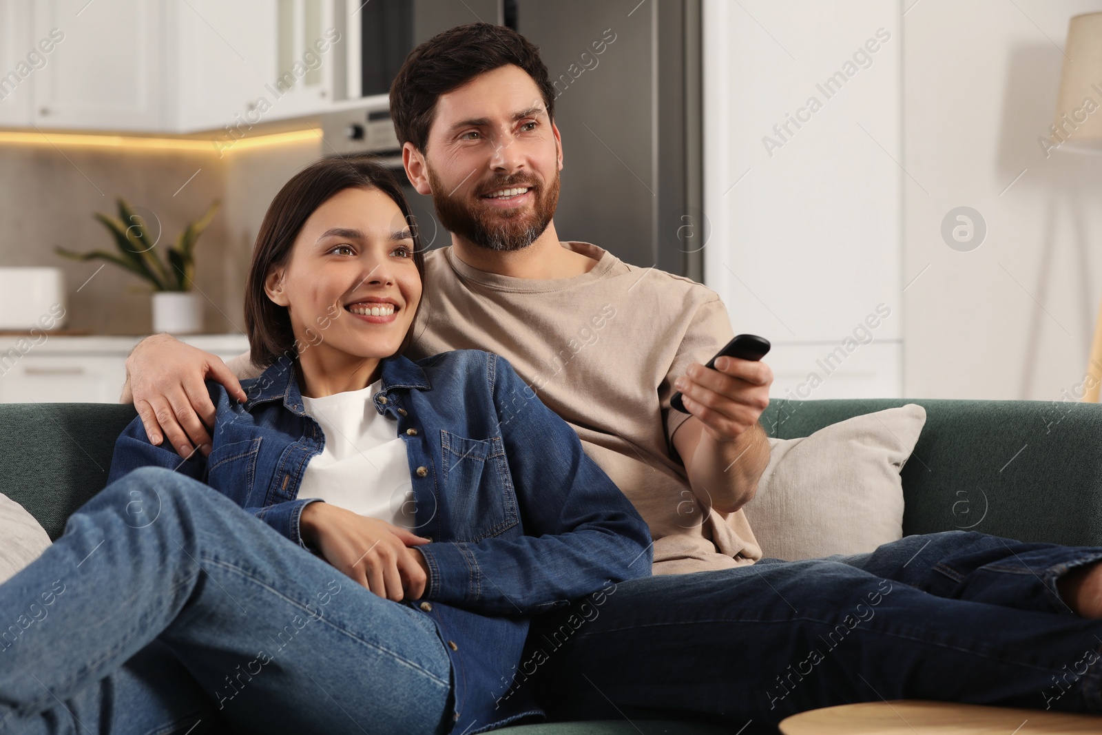 Photo of Happy couple watching TV on sofa at home