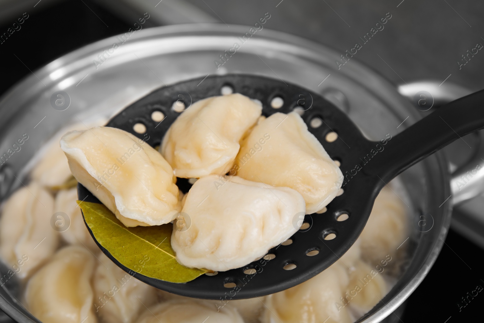 Photo of Dumplings (varenyky) with tasty filling on skimmer over pot indoors, closeup