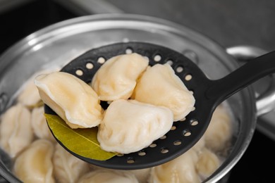 Dumplings (varenyky) with tasty filling on skimmer over pot indoors, closeup