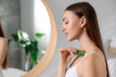 Photo of Young woman applying aloe gel from leaf onto her shoulder in bathroom. Space for text