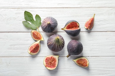 Flat lay composition with whole and cut purple figs on wooden background