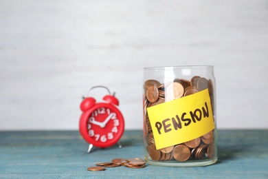 Photo of Coins in glass jar with label "PENSION" on table against light wall. Space for text