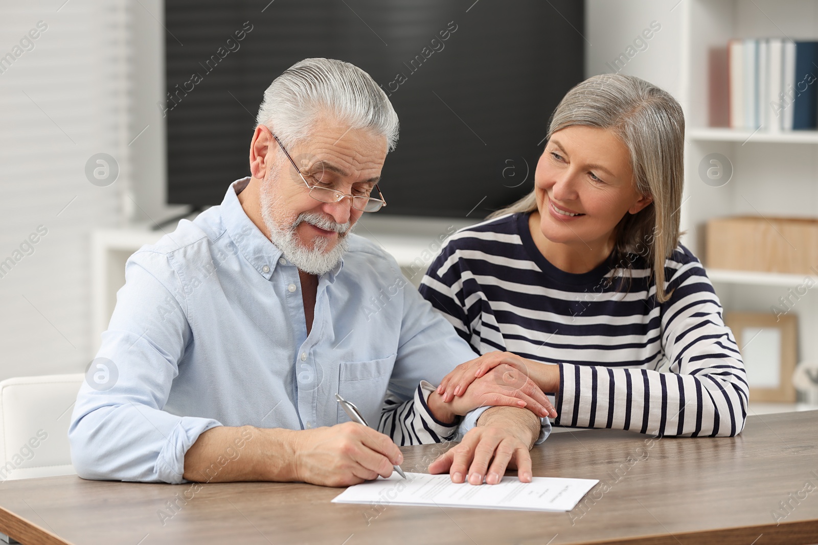 Photo of Happy senior couple signing Last Will and Testament indoors