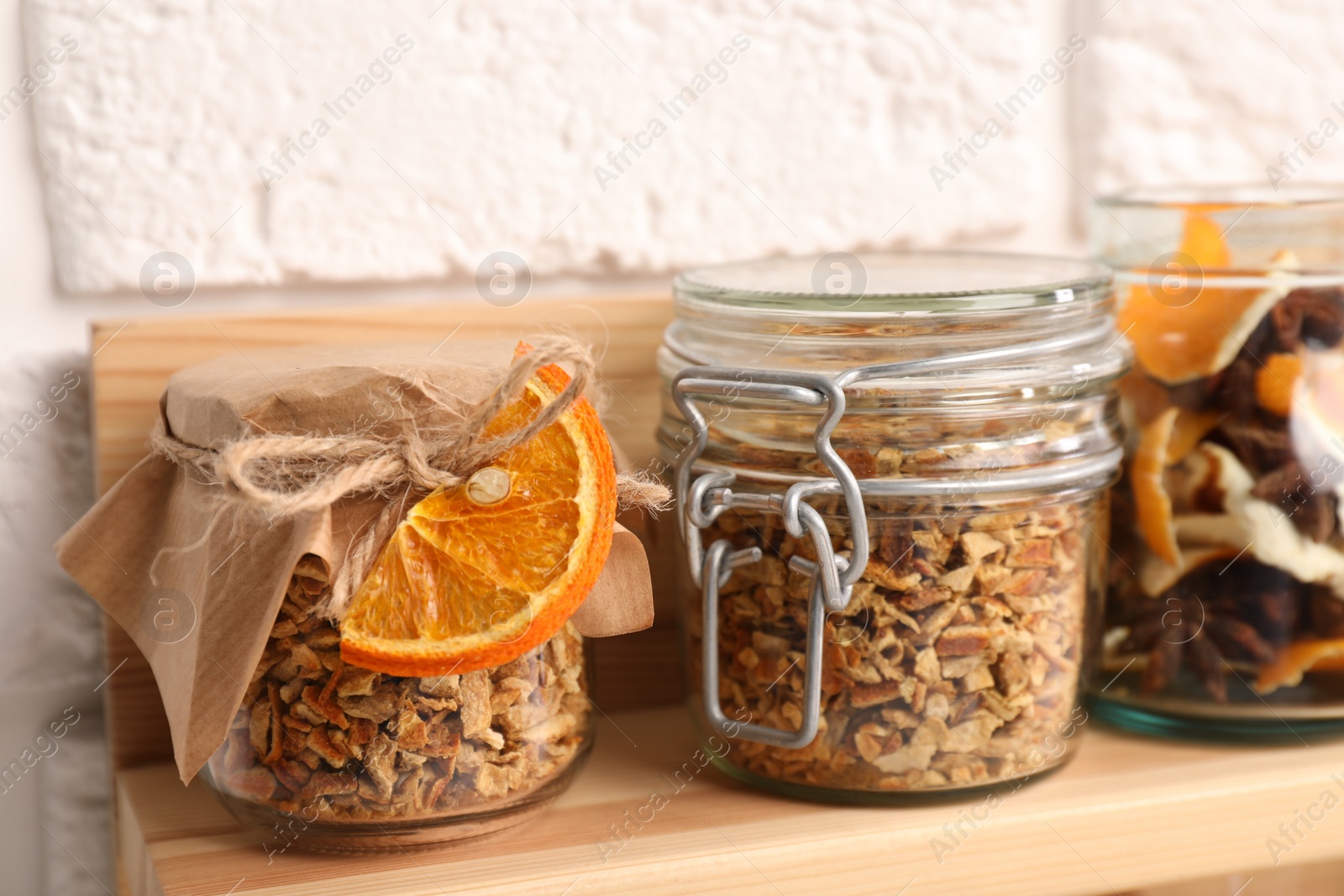 Photo of Jars of dried orange zest seasoning on wooden shelf near white brick wall