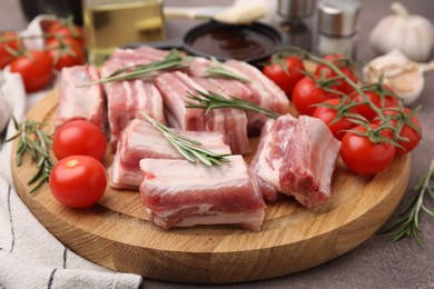 Photo of Cut raw pork ribs with rosemary and tomatoes on table, closeup