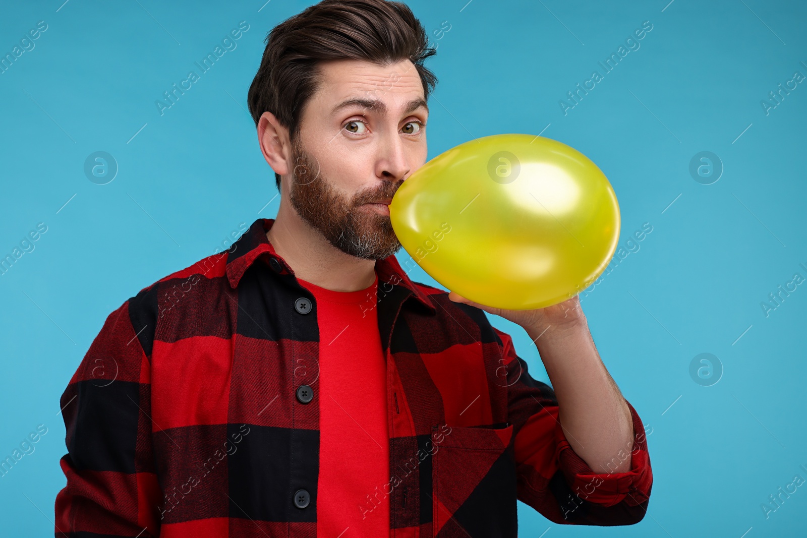 Photo of Man inflating yellow balloon on light blue background