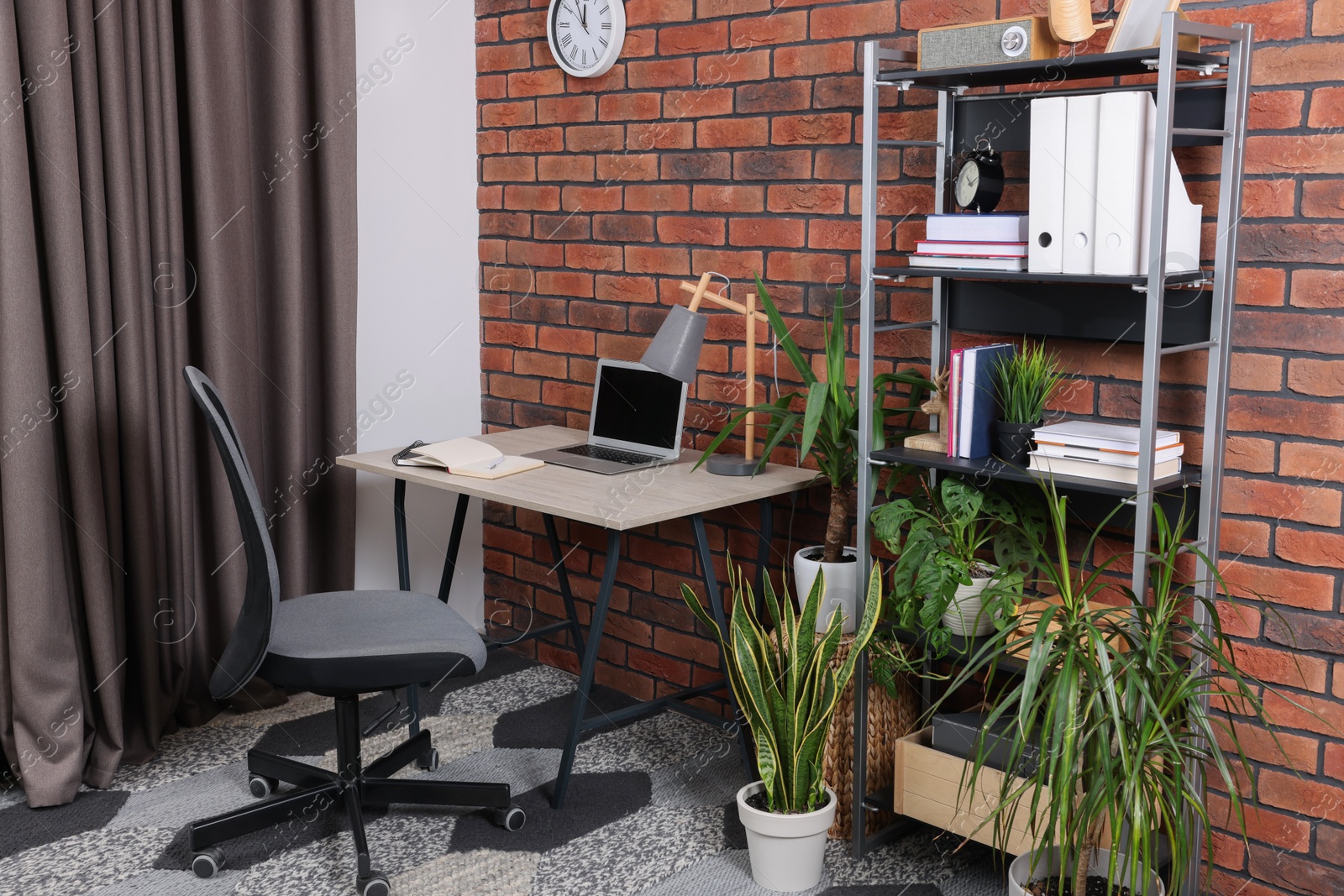 Photo of Stylish workplace with desk, chair, bookcase and potted plants at home
