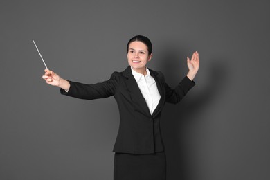 Happy professional conductor with baton on grey background