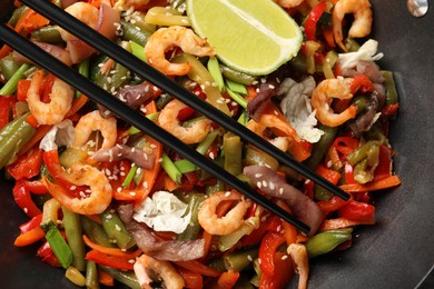 Shrimp stir fry with vegetables in wok and chopsticks on grey table