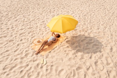 Woman resting under yellow beach umbrella at sandy coast