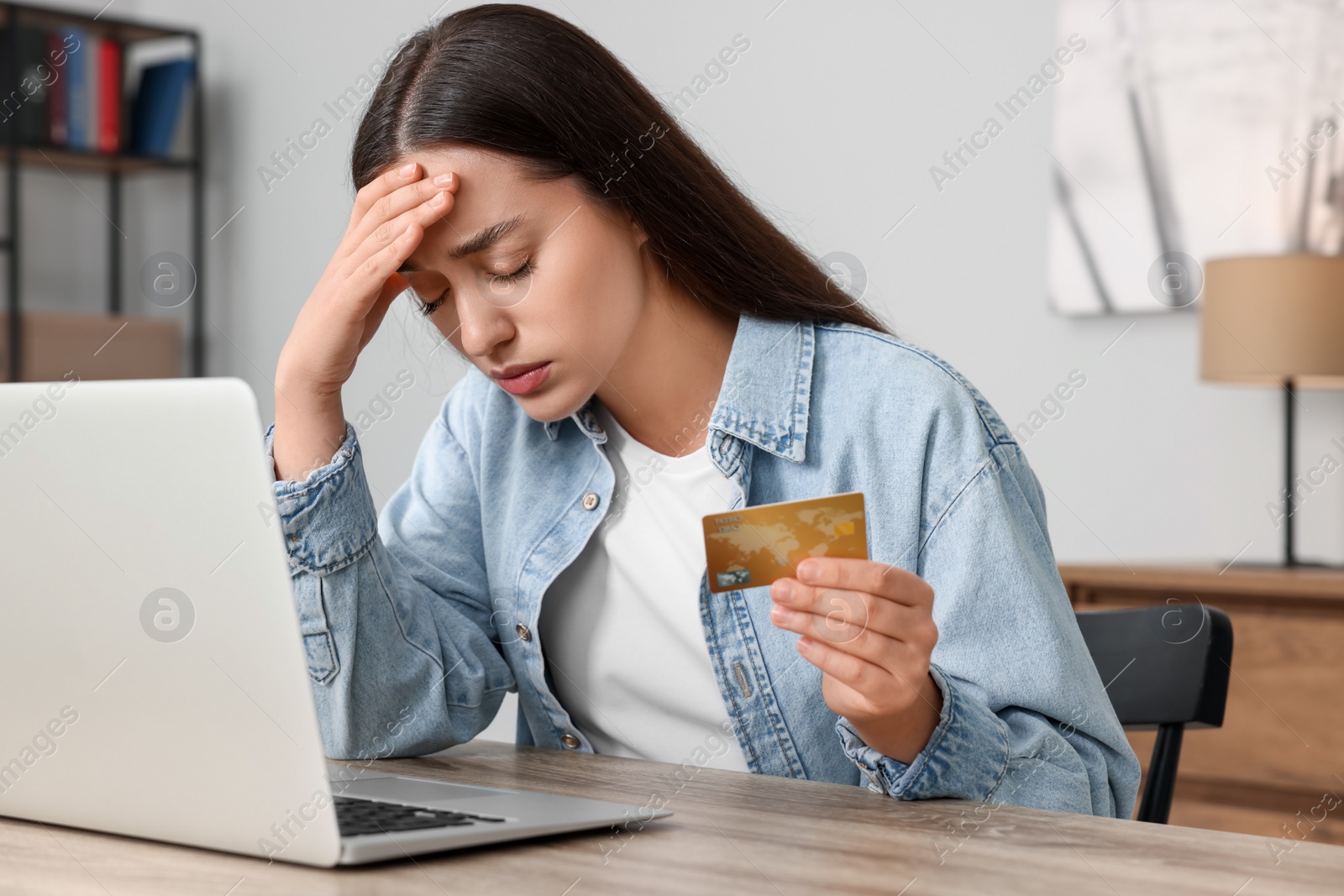 Photo of Stressed woman with credit card and laptop at table indoors. Be careful - fraud