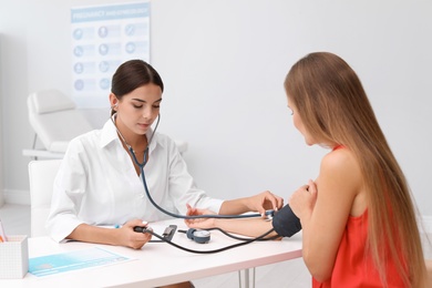 Photo of Doctor checking patient's blood pressure at table in office