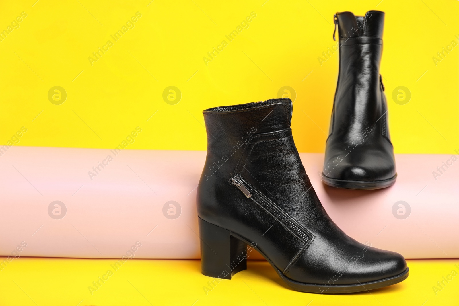 Photo of Stylish black female boots on yellow background. Space for text