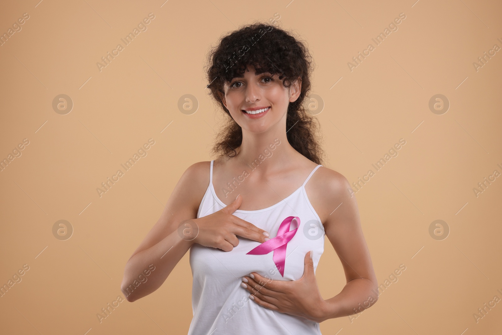 Photo of Breast cancer awareness. Smiling young woman with pink ribbon doing self-examination on light brown background