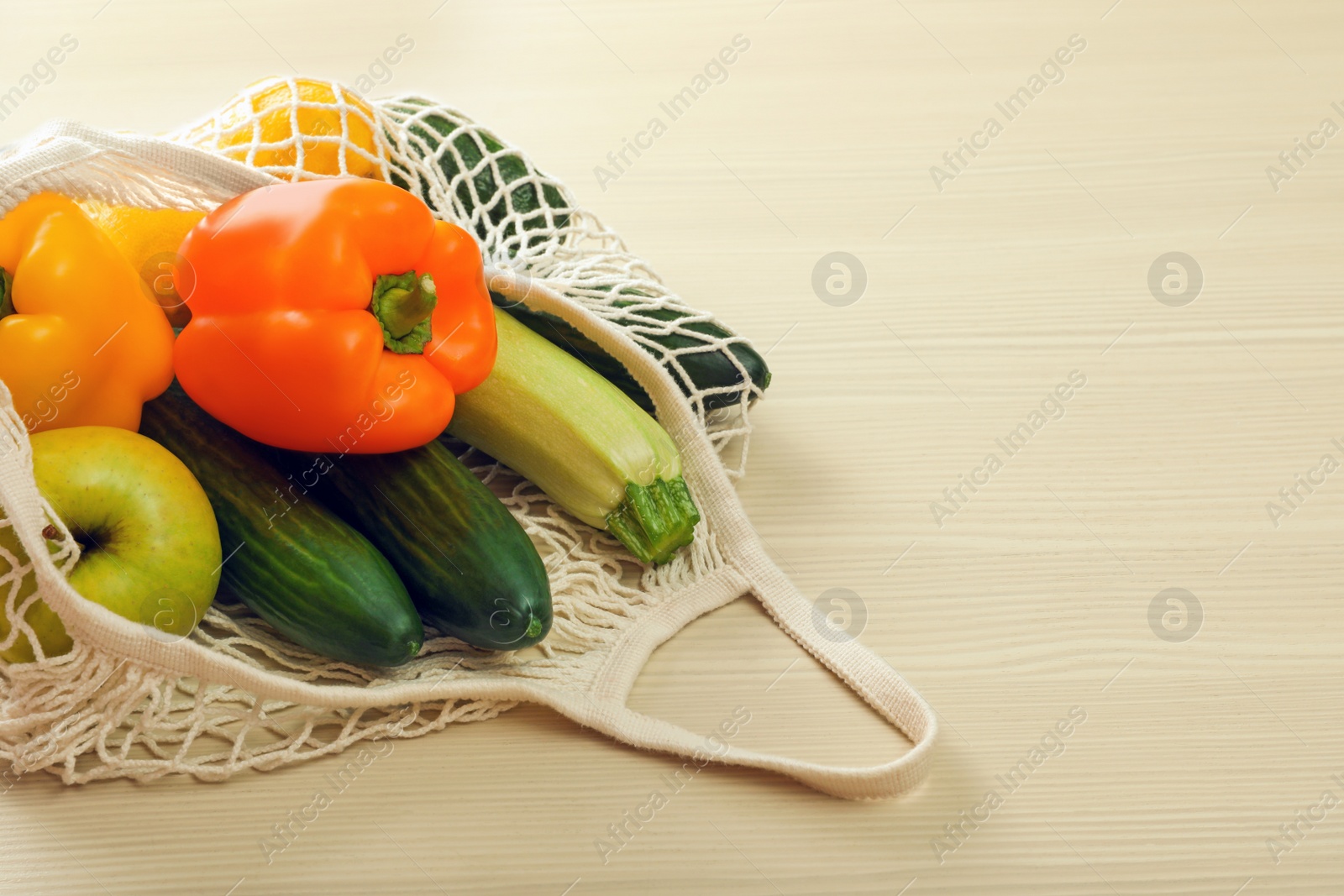 Photo of Net bag with vegetables and fruits on wooden table. Space for text