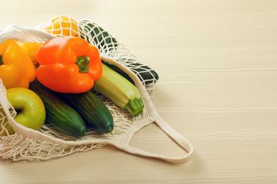 Photo of Net bag with vegetables and fruits on wooden table. Space for text