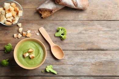 Photo of Flat lay composition with bowl of broccoli cream soup on wooden table, space for text