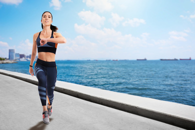 Athletic young woman running near sea on sunny day, space for text 